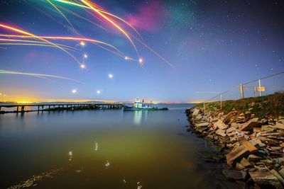 Fireworks over pier in river during night