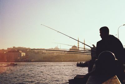 Man sitting on retaining wall by river against sky