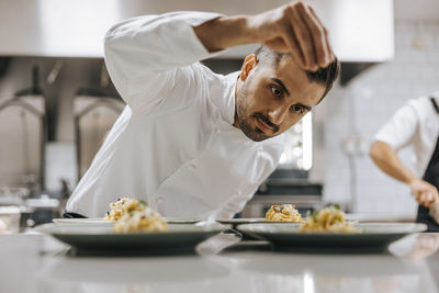 Young male chef sprinkling cheese on fettuccine pasta at kitchen counter in restaurant