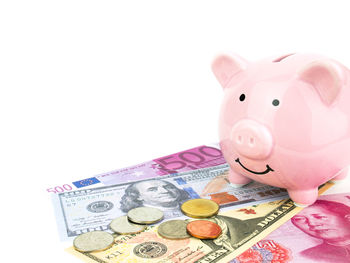 Close-up of piggy bank with currencies against white background