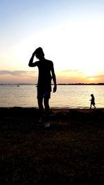 Silhouette woman standing on beach against sky during sunset