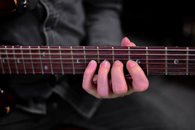 Close-up of woman playing guitar against black background