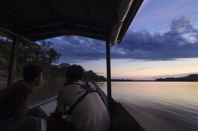 Rear view of men traveling through boat in tambopata river against sky