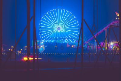 Illuminated ferris wheel against blue sky at night