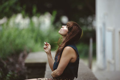 Woman smoking cigarette while sitting on retaining wall
