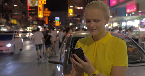 Midsection of man using mobile phone while standing in city at night