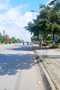 Road by trees in city against sky