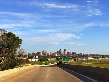 Road by buildings in city against sky