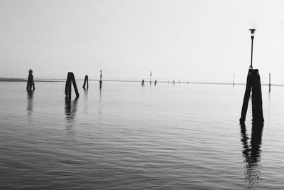 Silhouette people on wooden post in sea against clear sky