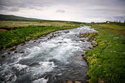 Scenic view of stream flowing amidst land against sky