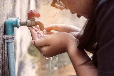 Cropped image of teenage girl drinking water from faucet