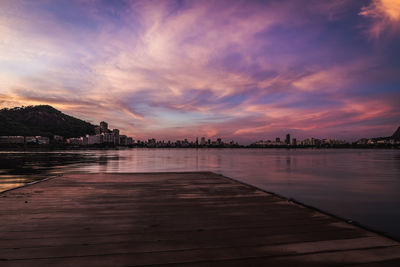 Scenic view of river by buildings against sky at sunset