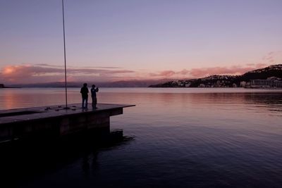 Silhouette people standing by lake against sky during sunset