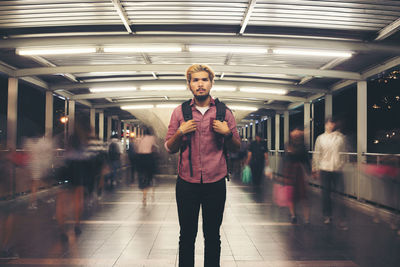 Portrait of young man standing on illuminated footbridge at night