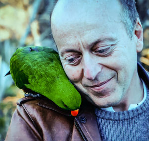 Close-up of smiling mature man carrying parrot on shoulder outdoors