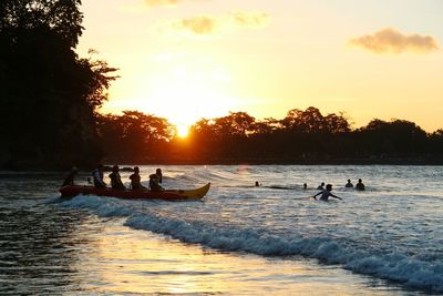 People enjoying in sea against sky during sunset