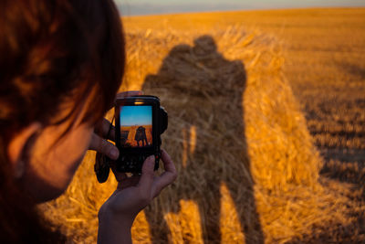 Woman photographing shadow of couple on hay during sunset