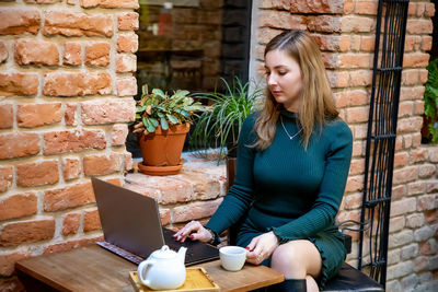 Young woman holding coffee while sitting on wall