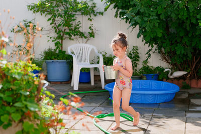 Cute young girl watering plants with a bucket on a summer day in the backyard