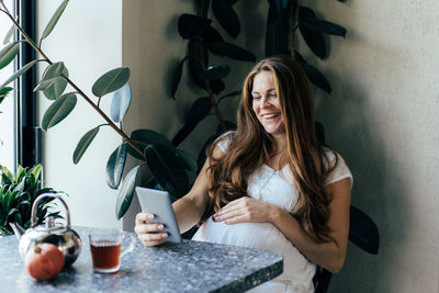 Cheerful happy laughing pregnant woman communicating by video call in tablet.