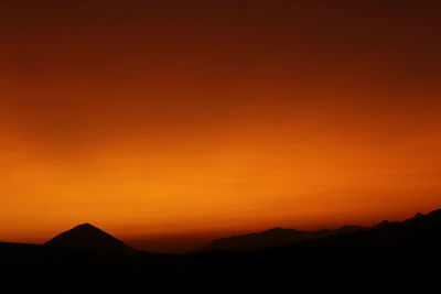 Scenic view of silhouette mountains against orange sky