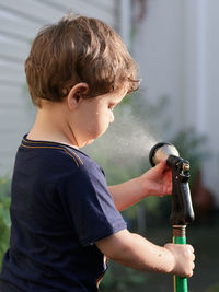 Little boy playing with a watering hose in the backyard