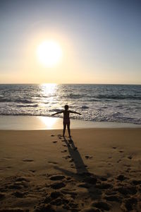 Silhouette man walking on beach against sky during sunset