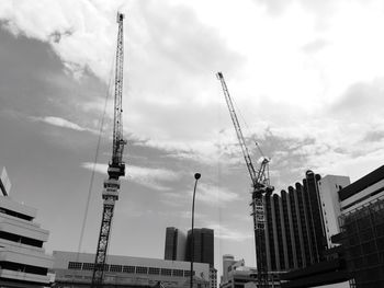 Low angle view of cranes against cloudy sky