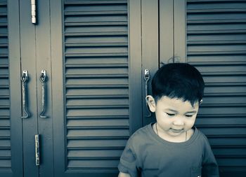 Cute boy looking away while standing against closed door