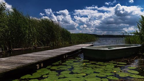 Boat moored on lake by jetty against sky