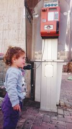 Side view of girl using telephone booth