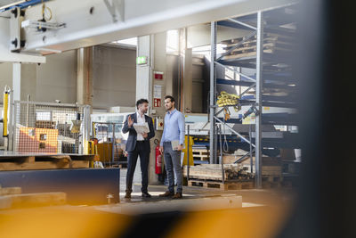 Young and mature businessmen having discussion while standing at factory