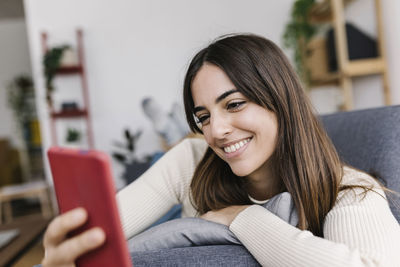 Happy woman text messaging through smart phone in living room