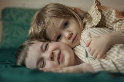 Portrait of smiling children lying on bed at home