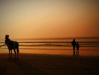 Silhouette man riding horse on beach against sunset sky