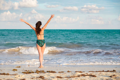 Rear view of woman standing at beach against sky