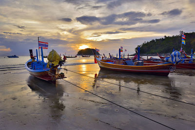 Boats moored on beach against sky during sunset