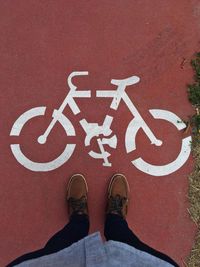 Low section of man standing by road marking on bicycle lane