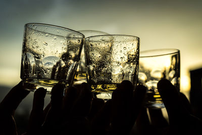 Cropped hands of friends toasting drinks against sky