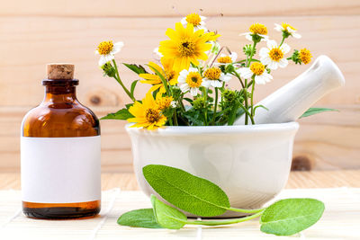 Close-up of flowers in mortar and pestle by bottle on table