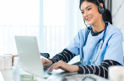 Smiling young woman using phone while sitting on table