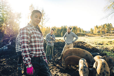 Portrait of mature female farmer with friends and pigs in background at organic farm