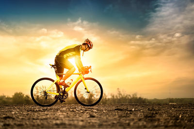 Man riding bicycle on road against sky during sunset