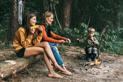 A young mother with her children is sitting by the campfire during a joint holiday