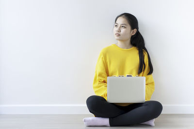 Young woman using mobile phone while sitting on wall