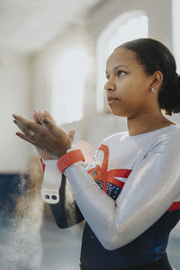 Female gymnast applying chalk powder on hands at gym