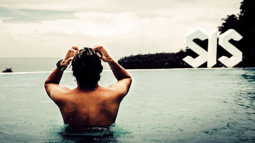 Rear view of shirtless man standing in swimming pool