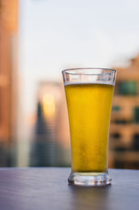 A glass of beer puts on table at rooftop bar with blurred city background.