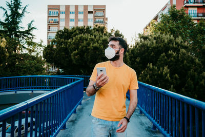 Young man using mobile phone while standing on railing