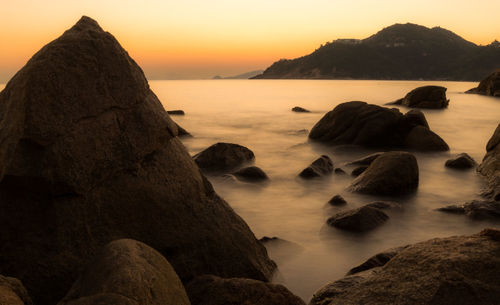 Rocks on sea shore against sky during sunset